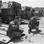 A black-and-white photo of U.S. Marines eating canned food behind a line of tanks