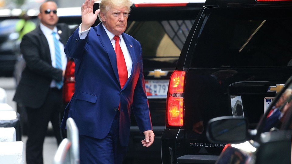 Donald Trump in a blue suit and red tie, waving
