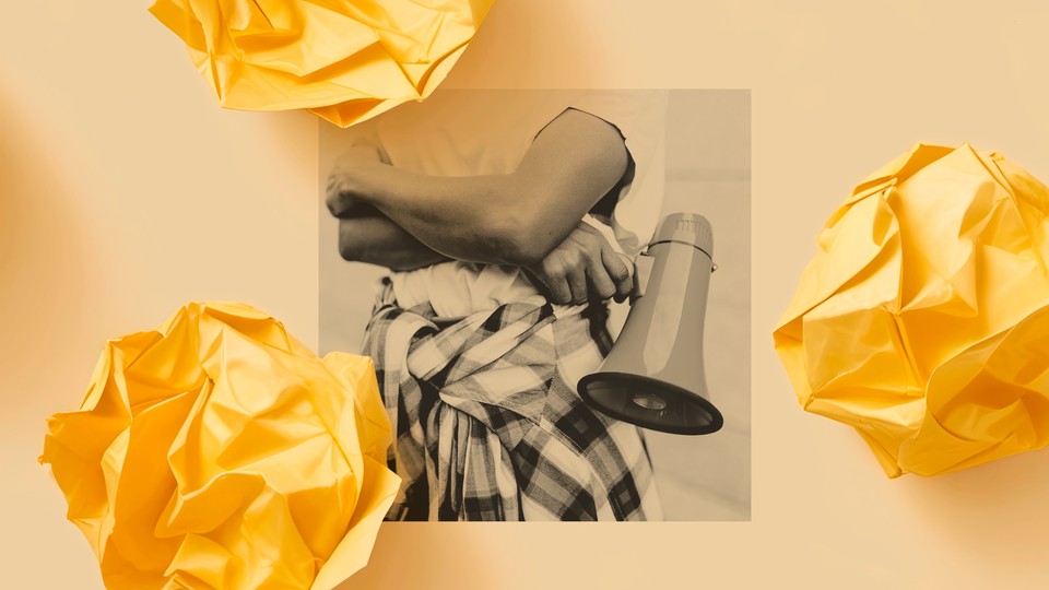 A black-and-white photo shows a person standing with their arms crossed and a megaphone in one hand.