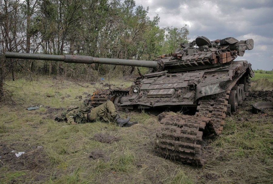 The body of a soldier lies near a destroyed tank.