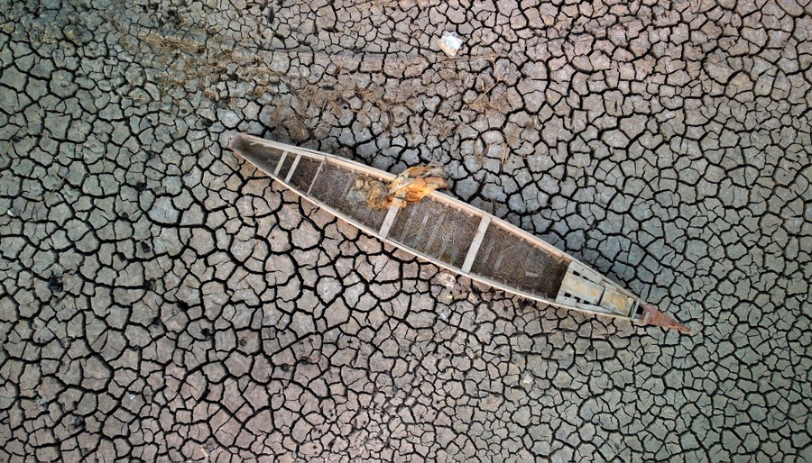 An aerial view of a boat stranded on cracked, dried-up, marshland