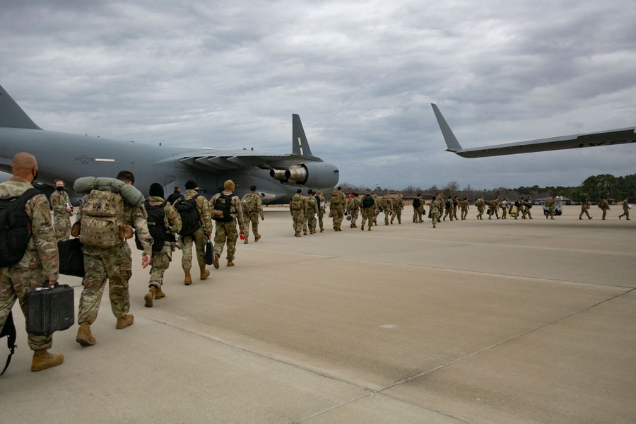 A line of dozens of U.S. troops walk in a line on pavement toward military aircraft.