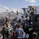 Color photograph of a crowd of Palestinians receiving aid from a convoy of trucks in Gaza