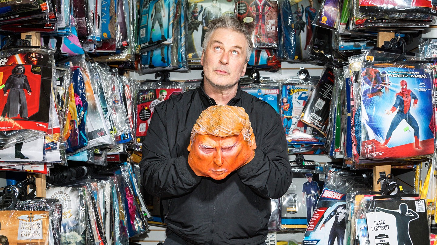 a portrait of Alec Baldwin holding a Trump mask