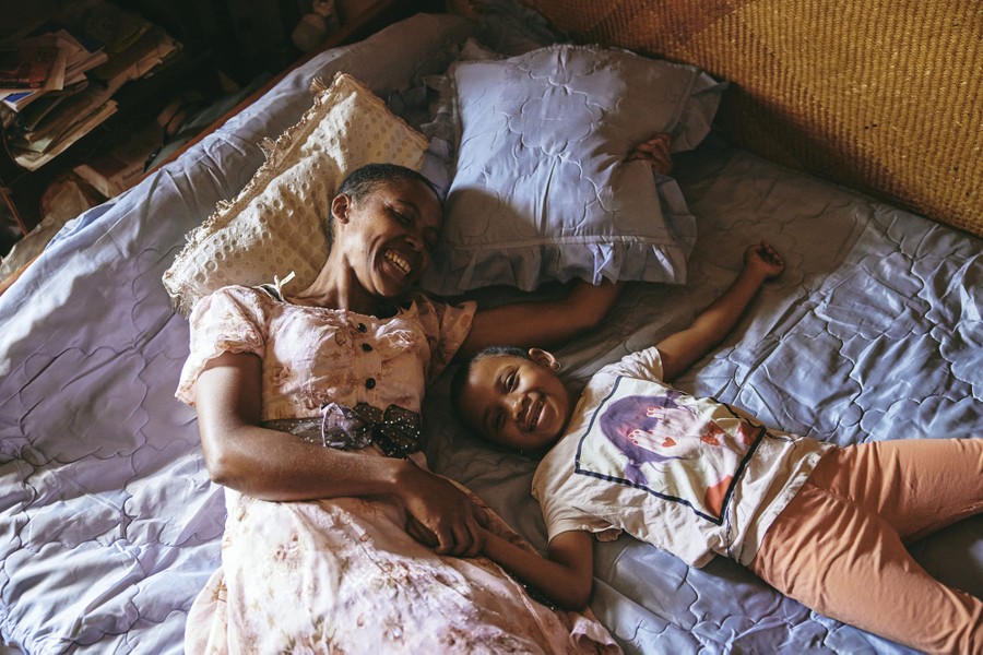 A mother and daughter smile while lying on a bed together.
