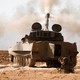 A Hezbollah fighters kneels next to a tank after firing his weapon in Syria