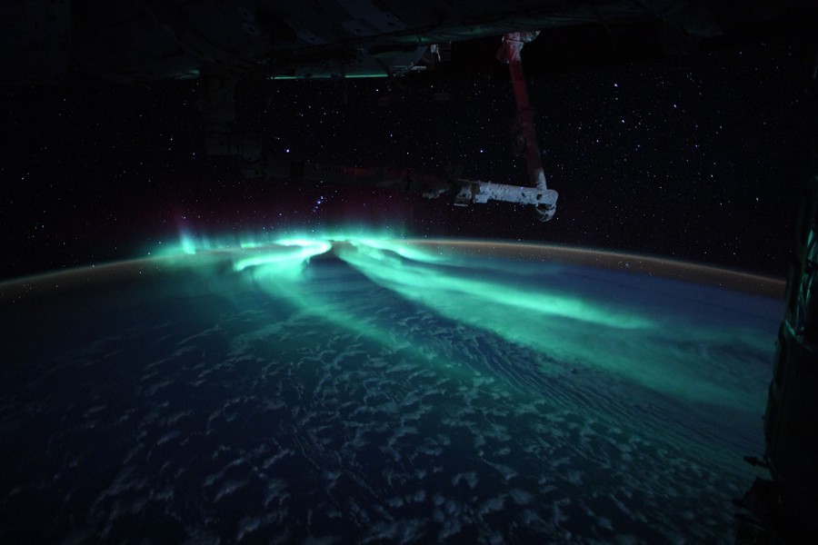 Moonlight illuminates clouds seen below a greenish aurora.