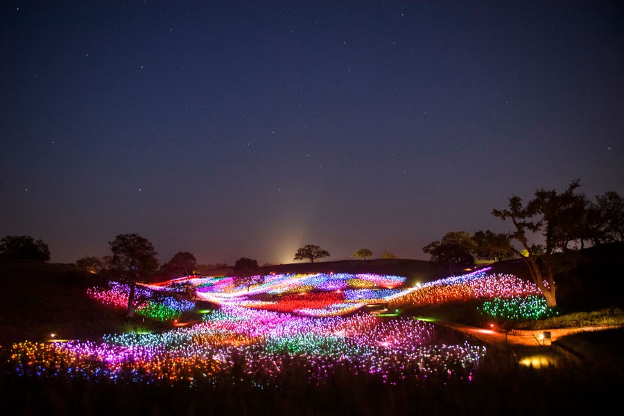 Brightly-colored lights flow over gentle hills, seen at night.