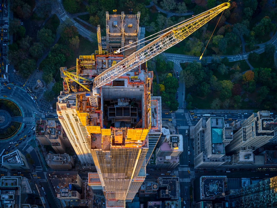 aerial photo looking down on supertall being built, with yellow crane and scaffolding on top of roof 