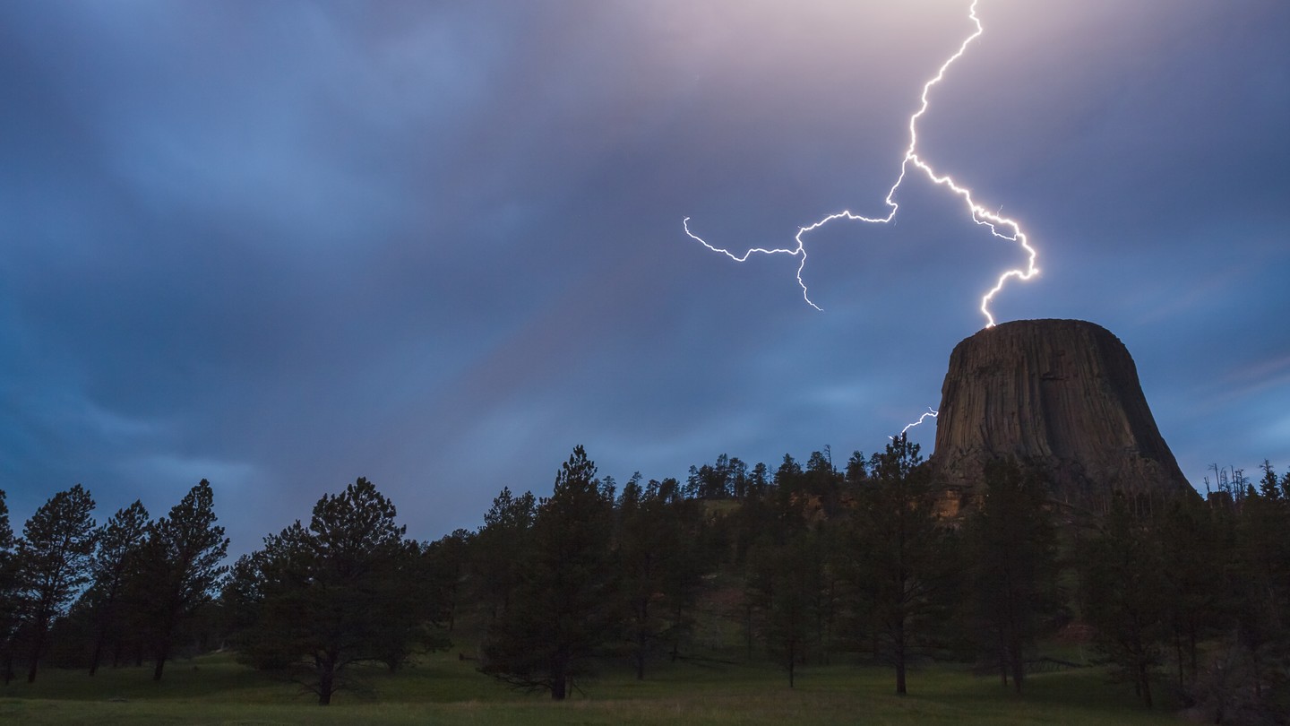 Lightning strikes near a tall, cylindrical rock formation.