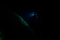 The lights of a submarine shine on a rock deep underwater.