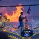 A protester carrying a Nepalese flag hangs a pirate flag on an ornate gate, as smoke and flames rise from a palace building in the background.