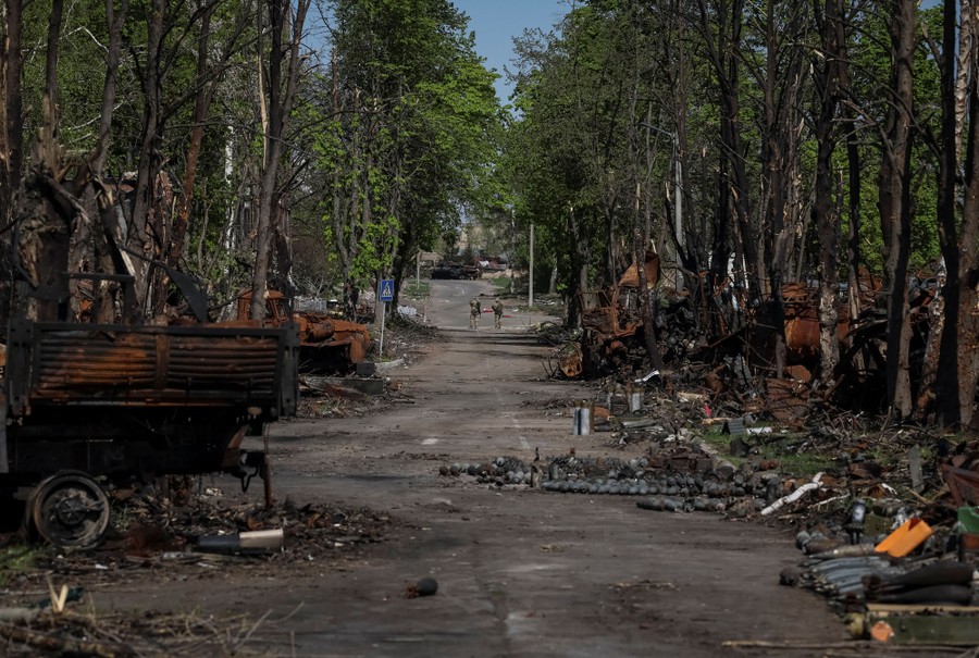 A tree-lined street is covered with debris from destroyed vehicles.