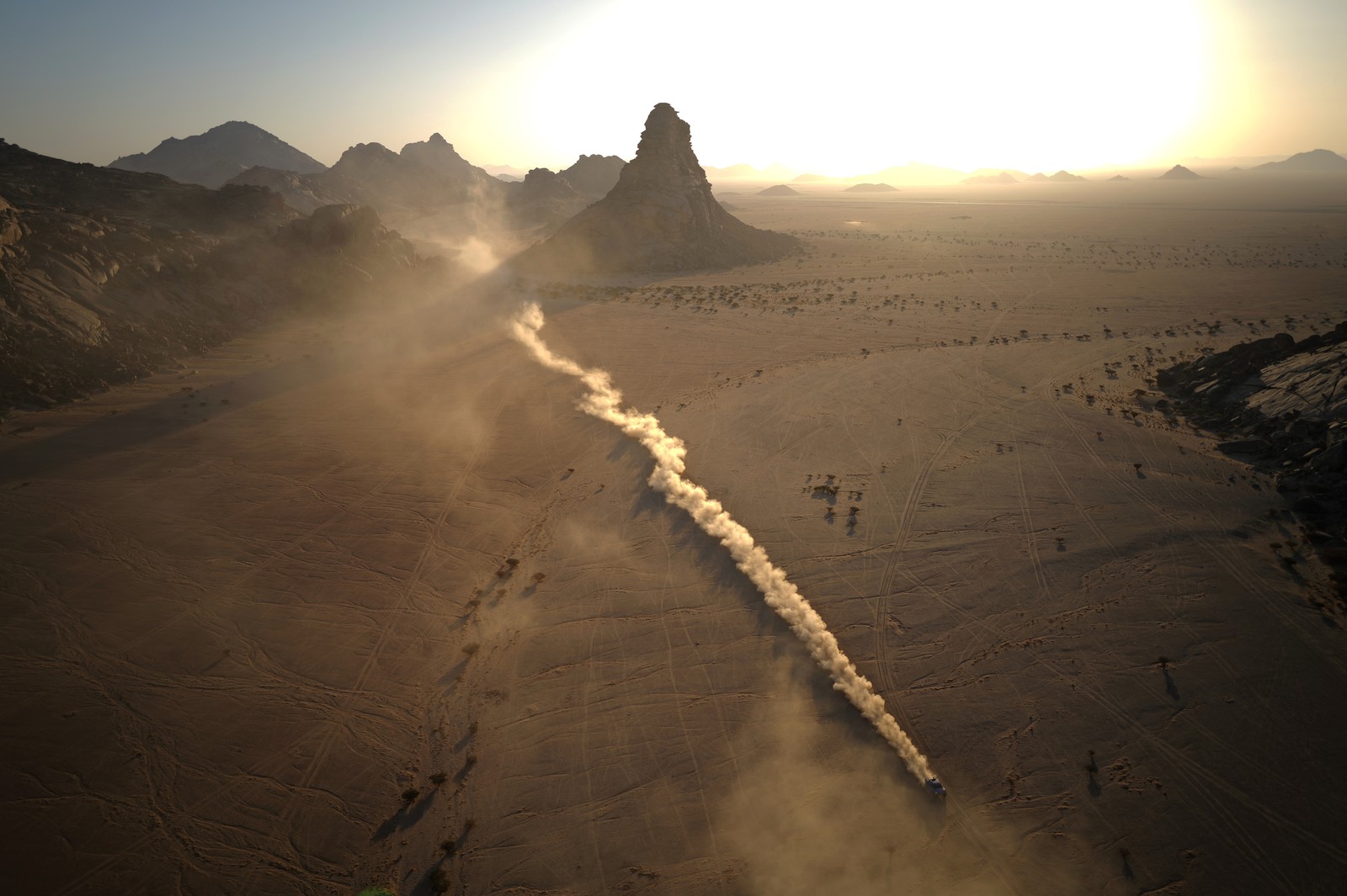 An aerial view of a rally racer leaving a long trail of dust across a desert.