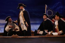 Four men on a boat in Revolutionary War clothing with an old American flag and a deep-blue stage backdrop