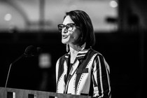 A black-and-white photo of Peggy Flanagan speaking at a podium