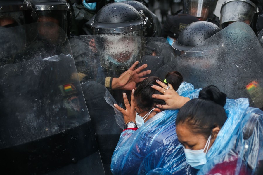 Several people raise their hands as they move in front of a group of riot police holding shields.