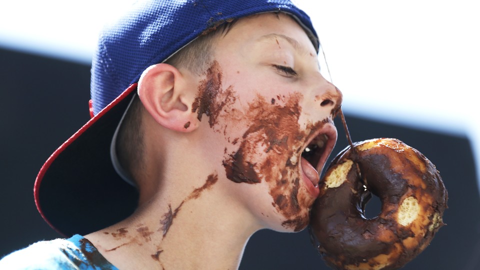 A boy with chocolate frosting all over his face, eating a donut