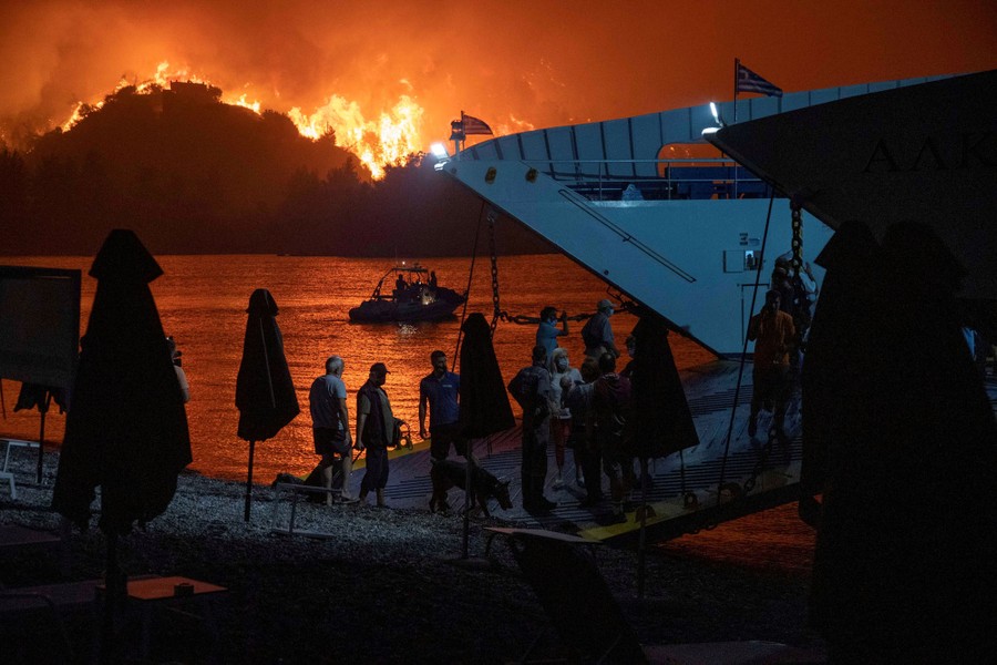 People board a ferry during an evacuation as a wildfire burns on nearby hillsides.