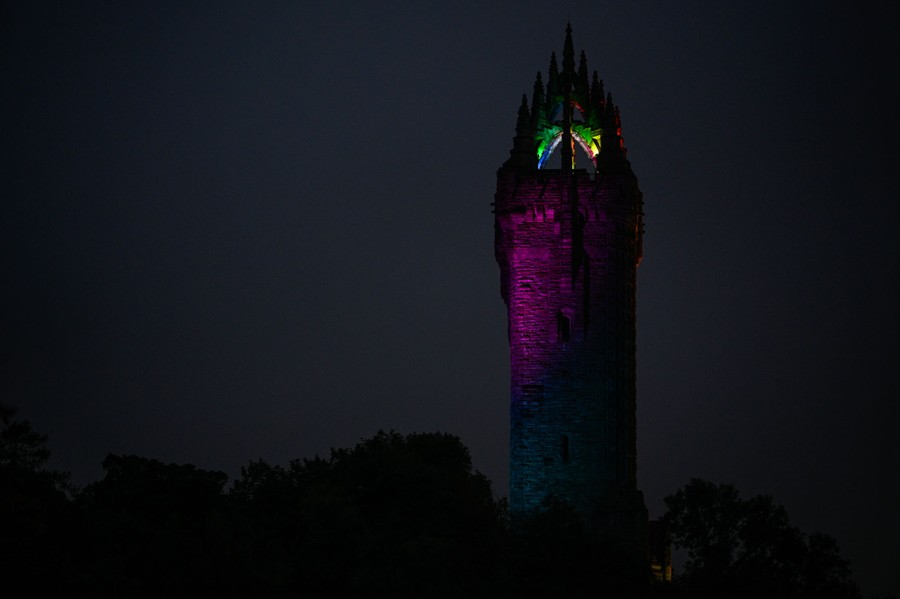 A tall stone tower is partly illuminated with multicolored lights.