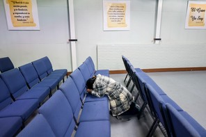 A woman on her knees and praying amid rows of blue chairs.