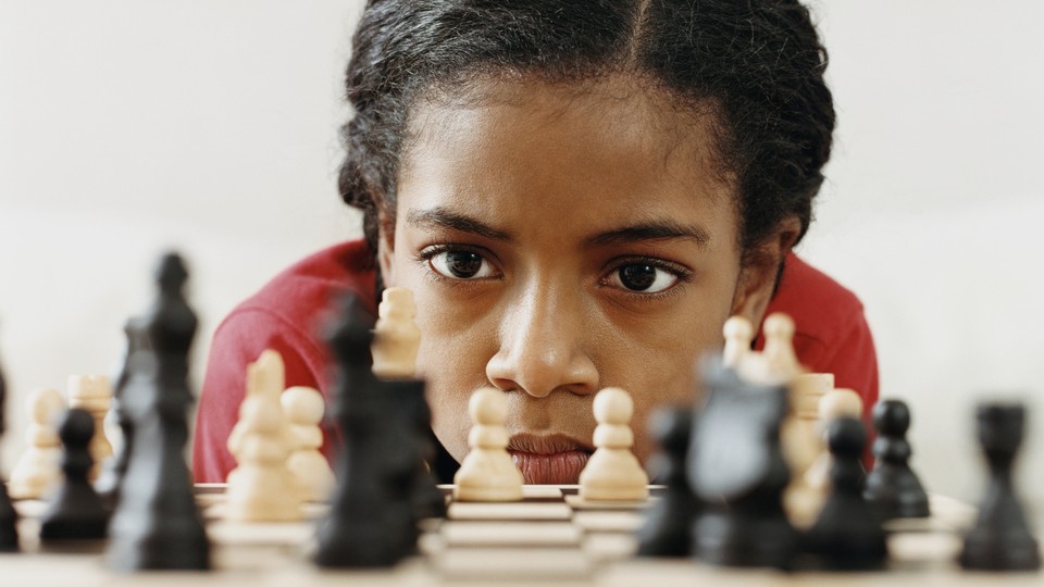 A young girl studies a chess board intently.