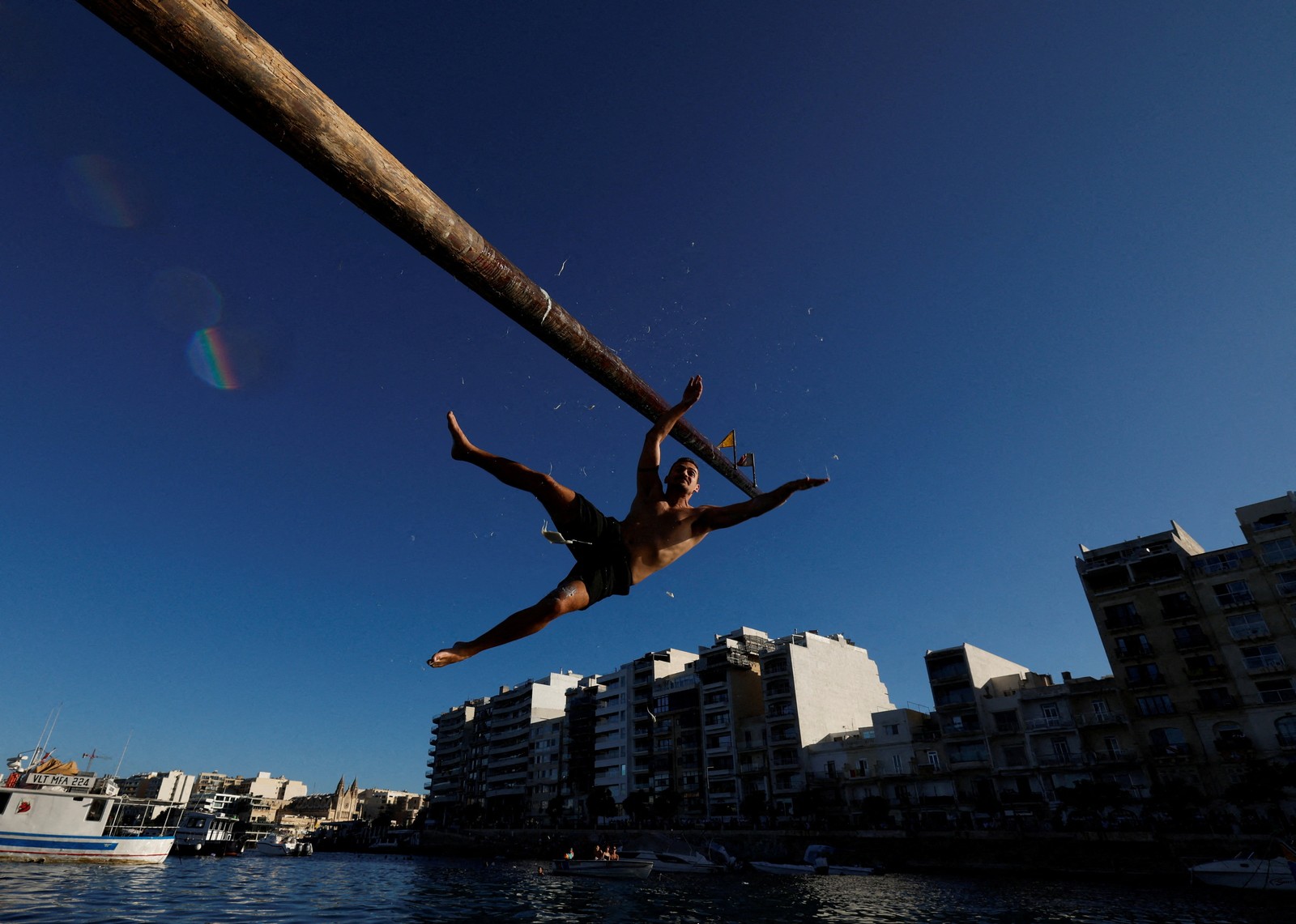 A person falls into the water of a harbor, after falling off of a greased pole during a festival.