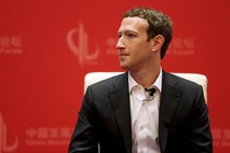 Mark Zuckerberg sits on a chair against a red background.