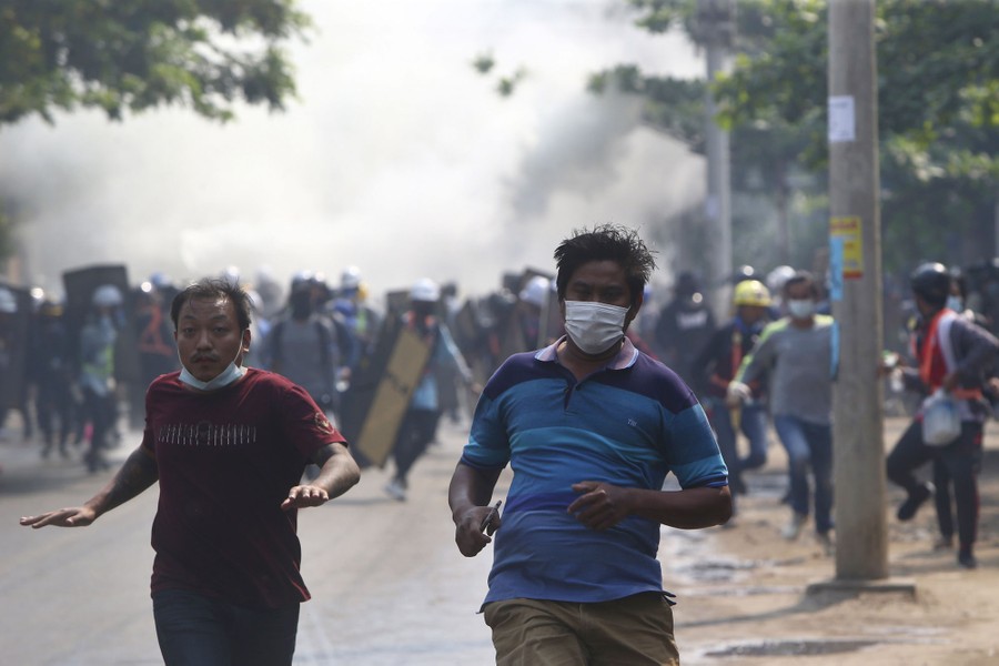 People run toward the camera, away from a cloud of gas, in a city street.
