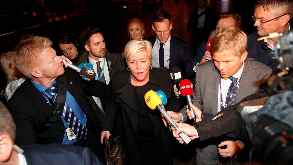 Siv Jensen walks out surrounded by reporters with microphones.