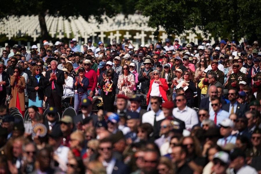 A crowd stands, waiting, beside a large military cemetery.