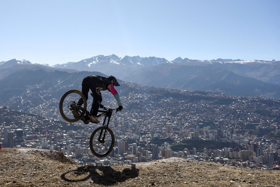 A cyclist descends a slope, with city buildings in the valley below.