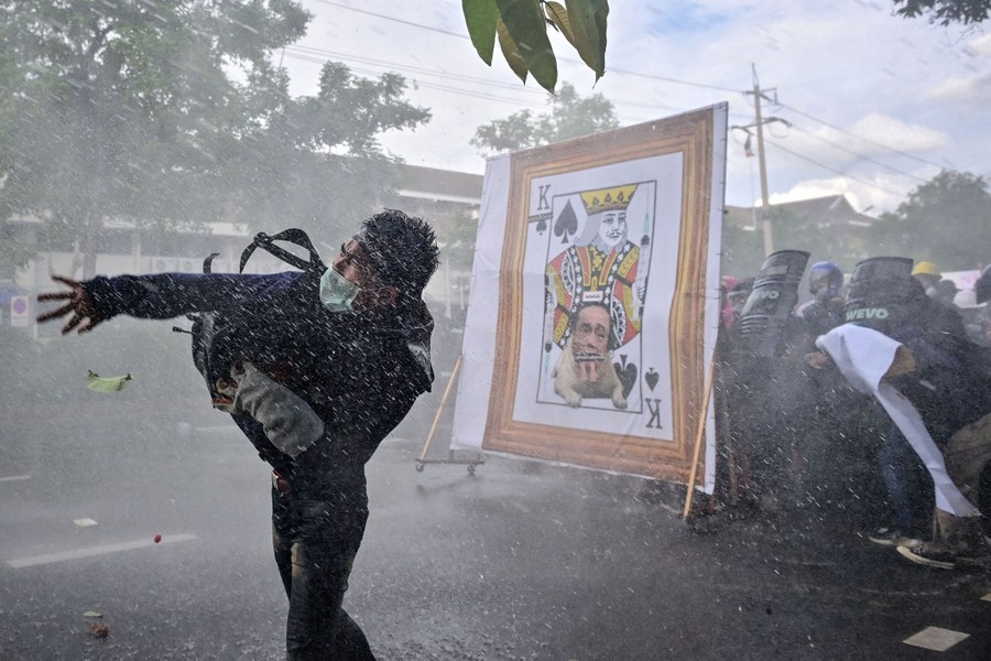A protester throws an object near others who take cover from a water cannon.