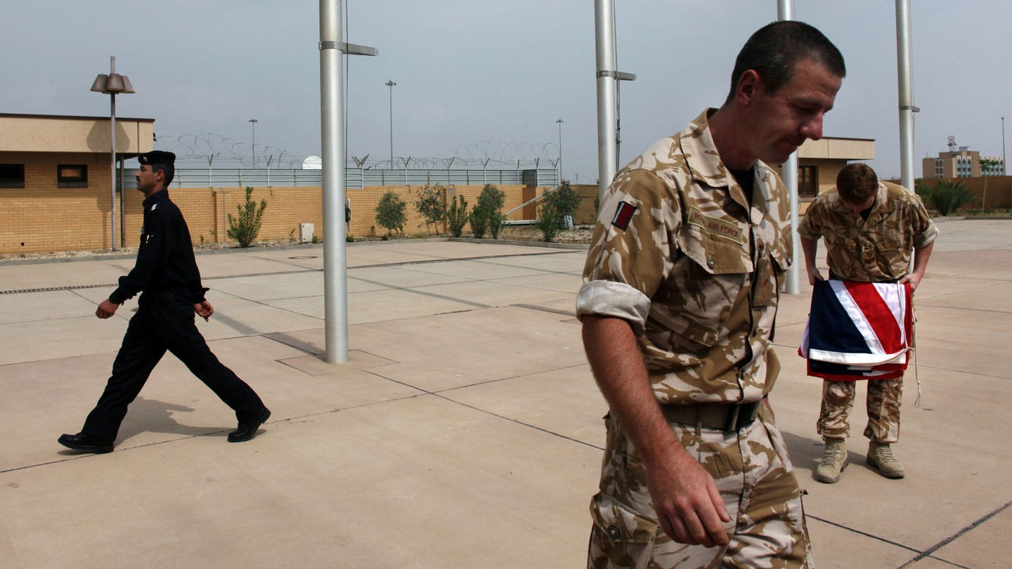 An Iraqi policeman walks past two British military officers, one folding the Union Jack.