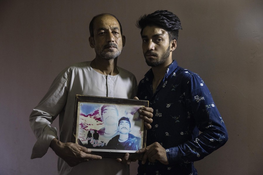 An Afghan father poses with his son and a portrait of another son who was killed.