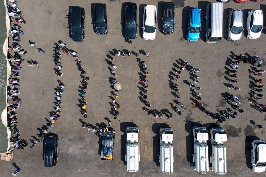 An aerial view of people standing in a long line in a parking lot.