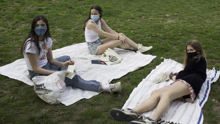Three teenagers wearing masks sit apart on picnic blankets.