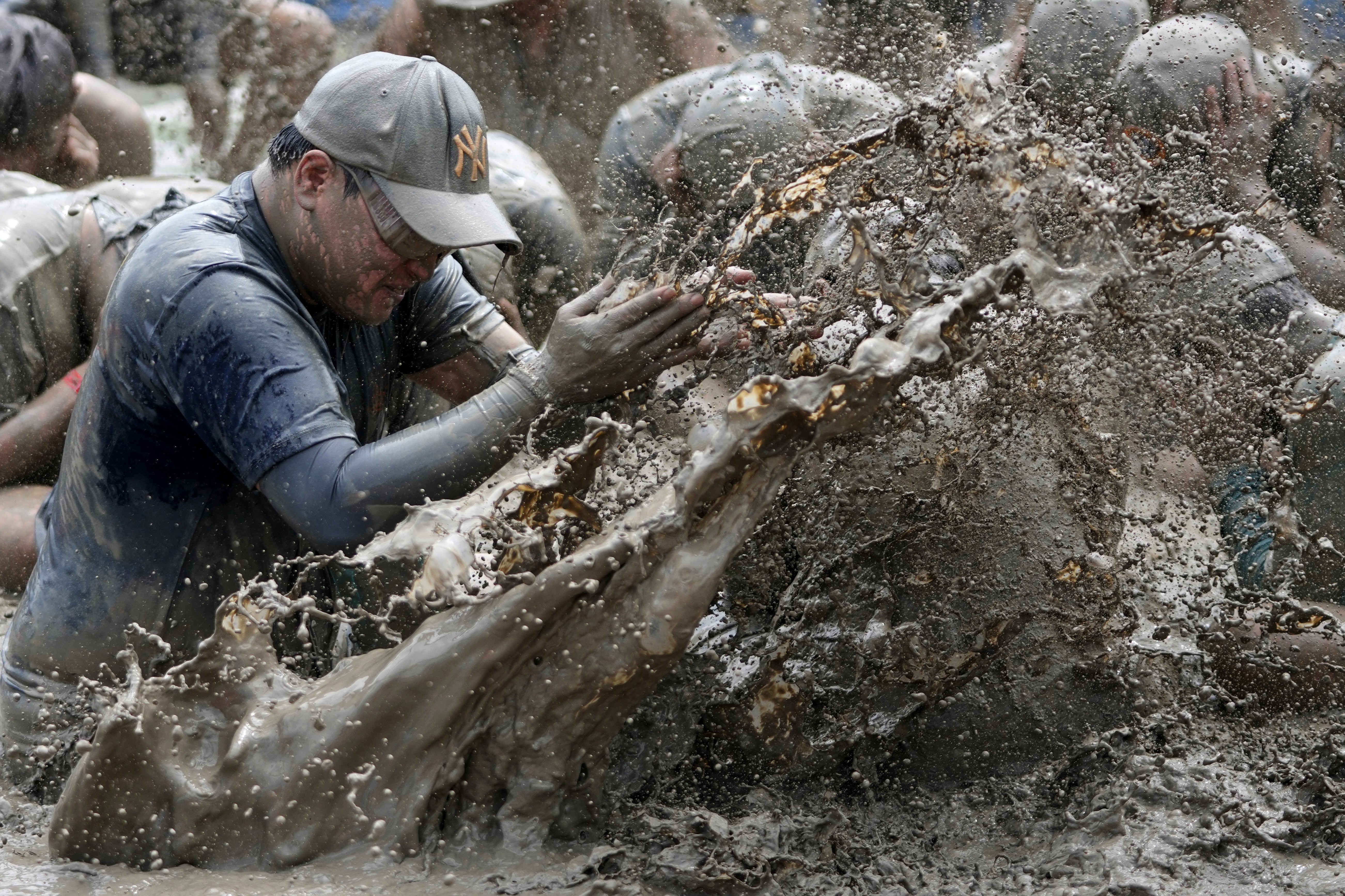 People play in a mud pool, splashing each other.
