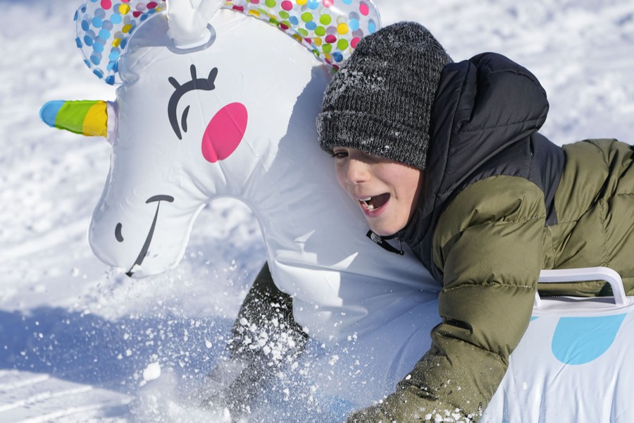 A young person sleds down a hill on an inflatable unicorn.