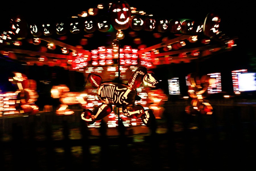 A carousel made of pumpkins is illuminated at night, with skeletal "horses" set up on poles.