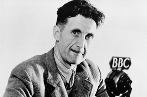 A black-and-white portrait of George Orwell in 1943 in front of a microphone with a "BBC" tag