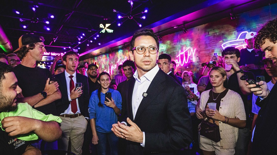 James Fishback looks to the side of the camera as he is surrounded by a crowd of people holding phones and cameras towards him