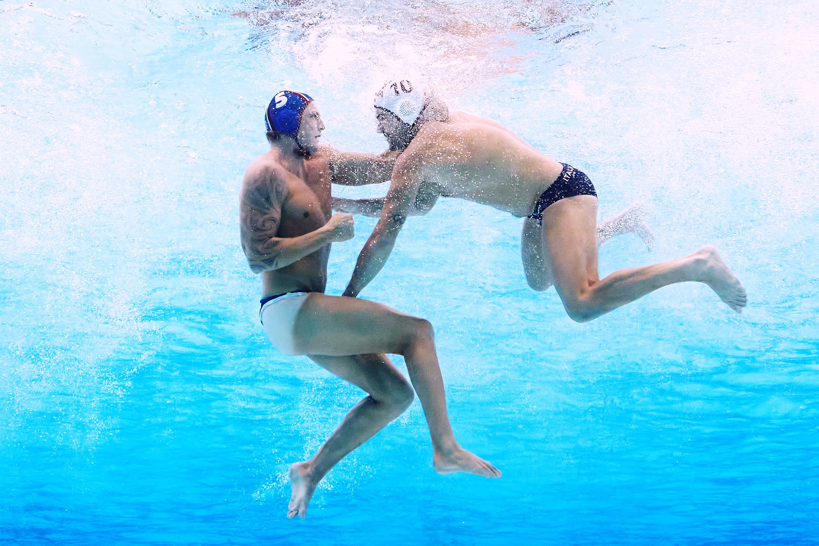 Two water polo players clash underwater, one appears to be grabbing the swimsuit of the other.