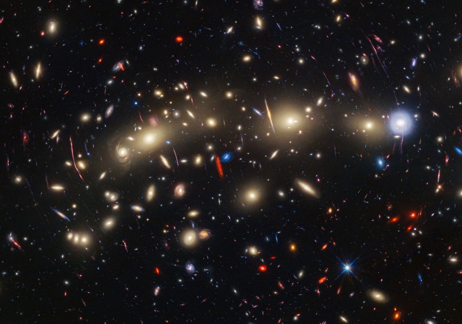 Dozens of distant galaxies, some stretched and distorted, appearing as thin lines or smears