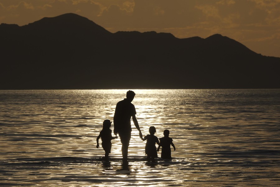A family walks in shallow water at sunset.