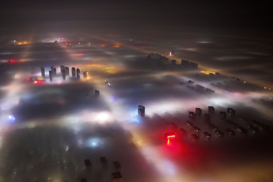 An aerial view of residential and commercial buildings blanketed in thick fog at night