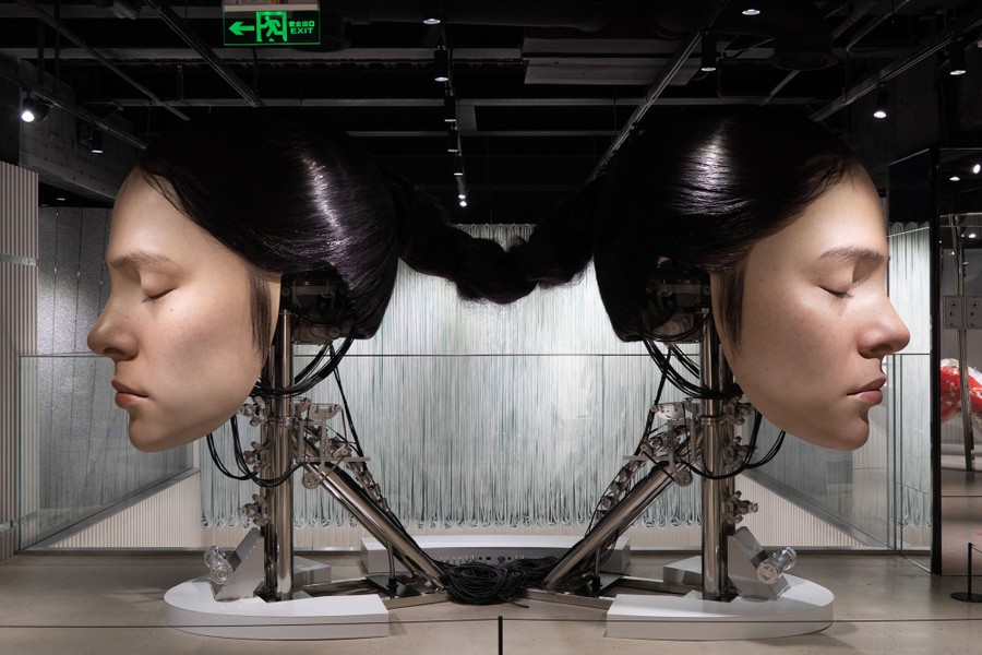 A large art installation made up of two human-shaped heads, their long ponytails bound together, atop complicated metal cylinders.