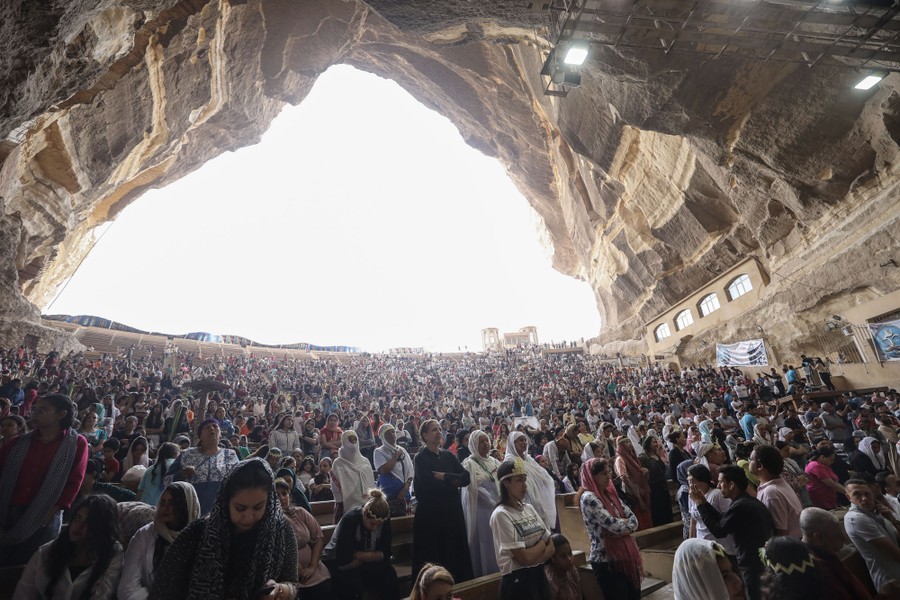 A crowd of people gather in a church set in a natural amphitheater inside the mouth of a large mountain cave.