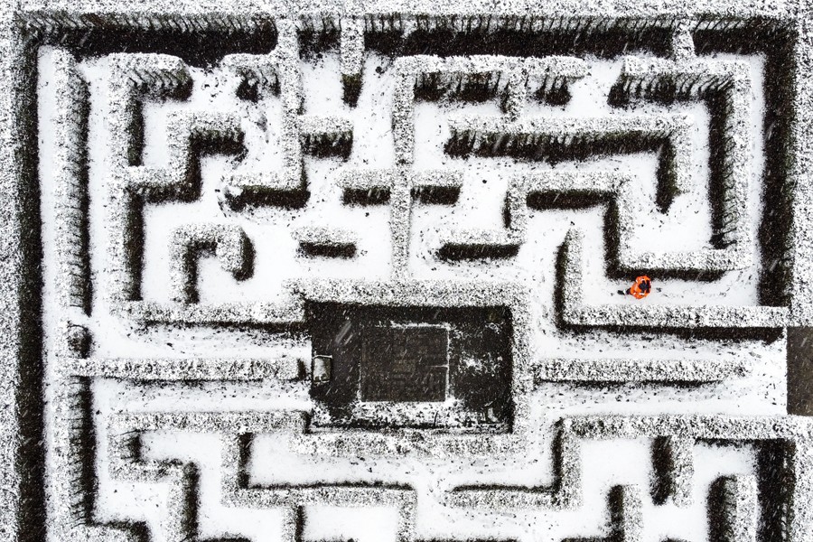 An aerial view of a gardener walking through a snow-covered hedge maze