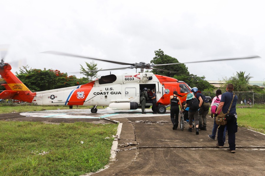 People are escorted to a U.S. Coast Guard helicopter on a pad.